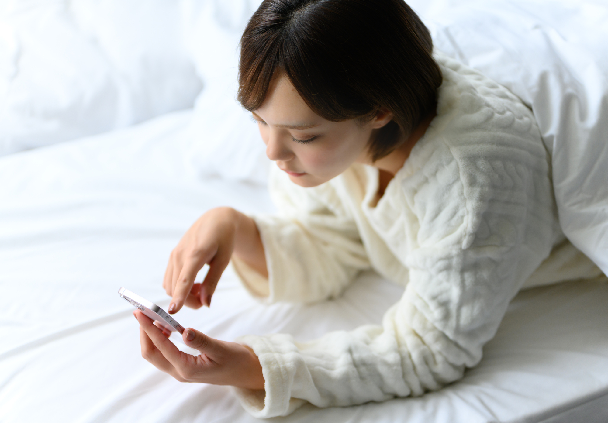 寝転んでスマホを見ている女性の画像